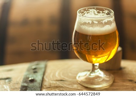 Glass of light barrel aged beer standing on an oak wood barrel Royalty-Free Stock Photo #644572849