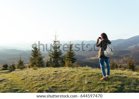 The girl walks through the mountains and takes a picture of the sunset