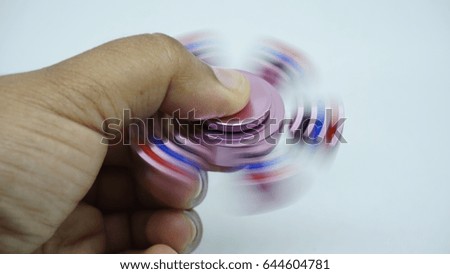 A hand held a pink metal Hand spinner. Fidget for increased focus, stress relief in white background. Image has blurry or soft focus when view at full resolution (Shallow DOF, slightly motion blur).