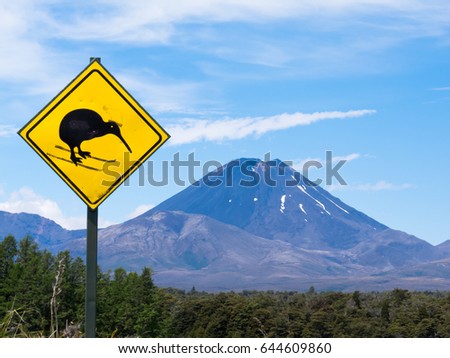 Active volcano Mount Ngauruhoe and modified Attention Kiwi Crossing Road sign on North Island of New Zealand