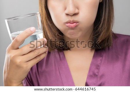 Woman rinsing and gargling while using mouthwash from a glass, During daily oral hygiene routine, Girl in a purple silk robe, Dental Healthcare Concepts Royalty-Free Stock Photo #644616745