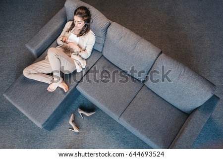 Overhead view of tired businesswoman resting on couch with smartphone at home 