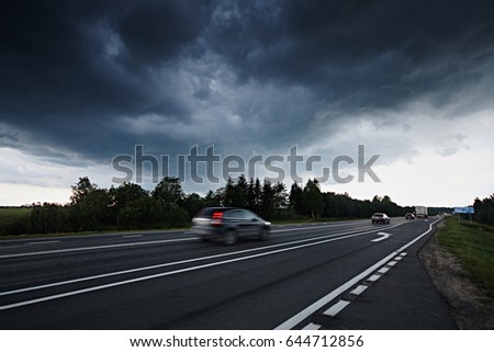 Asphalt road and a stormy dark blue sky. Cars go on the road and blurred