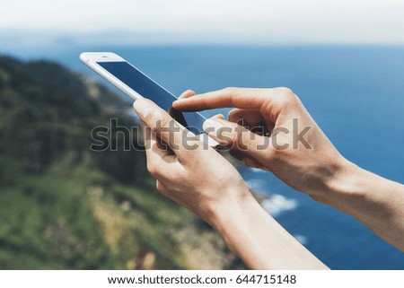 Hipster photograph on smart phone gadget mobile, mock up of blank screen. Traveler hold and using in female hand mobile on background mountain seascape horizon. Tourist look on blue ocean, lifestyle 