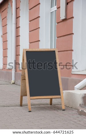An empty chalk board stands on the street next to the cafe. There is place for an inscription