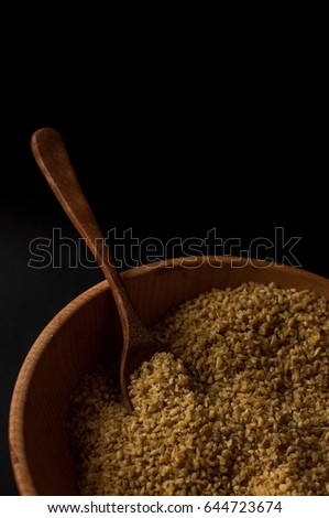 Dry bulgur wheat in brown wooden bowl isolated on dark wood.