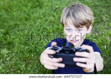 Child boy making selfie using a retro rangefinder camera outdoors. Little child blond boy with an old camera shooting photo of himself. Kid taking a photo using a vintage retro film camera. 