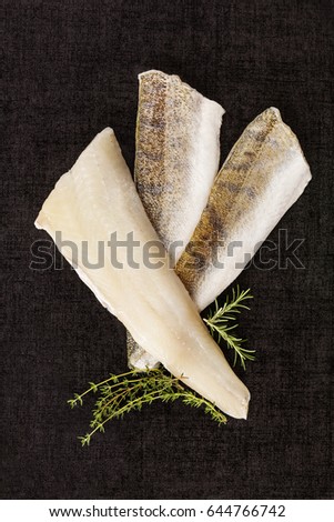 Fillet fish slices on green herbs isolated on black background, top view. Luxurious seafood eating. 