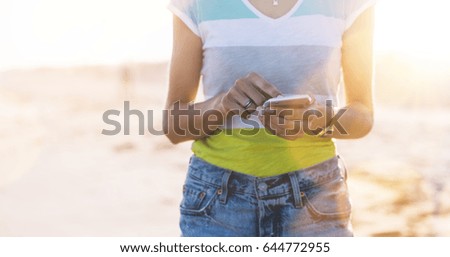 Hipster girl photograph on smart phone gadget in sand coastline beach, mock up of blank screen. Traveler hold and using in female hand mobile on background seascape horizon. Tourist lon blue sun ocean