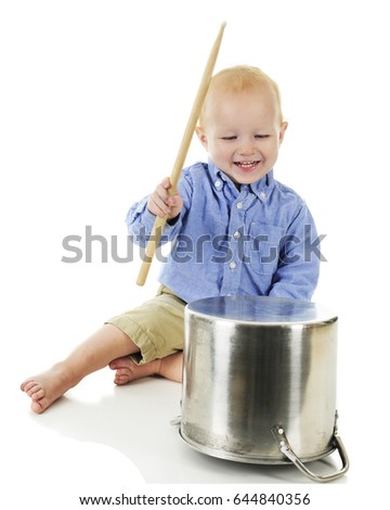 An adorable toddler boy delightedly banging away on a large crock pot with a wooden drumstick.  On a white background.