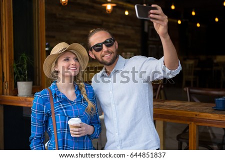 Smiling young couple taking selfie with mobile phone in coffee shop