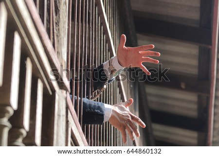 closeup on hands of man sitting in jail. Man behind jail bars on black background reaching