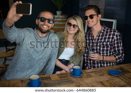 Happy man with friends taking selfie at table in coffee shop