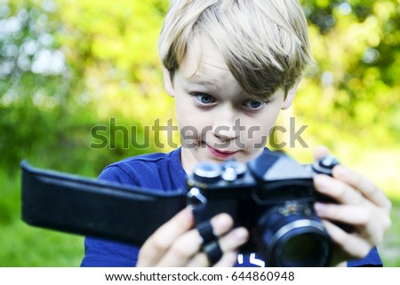Sad boy looking at the open back of the camera and enlightened ruined film inside. Little child blond boy with an old camera shooting outdoor. Kid taking a photo using a vintage retro film camera. 