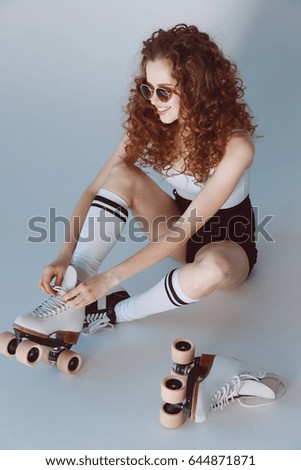 High angle view of hipster girl in sunglasses wearing roller skates sitting isolated on grey   