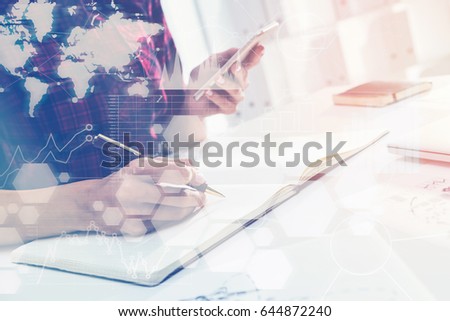 Close up of woman s hands writing in an office. She is holding her smartphone and planning a schedule. Elements of this image furnished by NASA. Toned image
