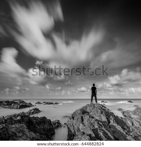 man standing on a rocky coastline, A slow shutter speed was used to see the movement ( Soft focus due to long exposure shot ) square format
