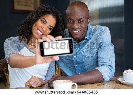 Smiling multi ethnic couple taking selfie with smart phone in coffee shop