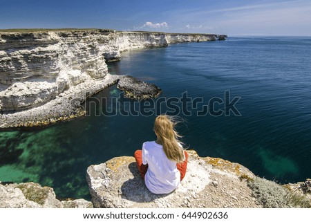 girl in white t-short sitting on a cliff near sea bay