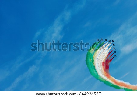 Air fighters on an air show flying in the shape of a geometric figure with colorful bright trails of smoke against a blue sky with clouds. Air performance Royalty-Free Stock Photo #644926537