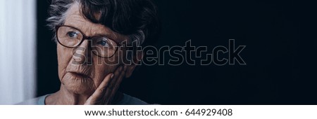 Elderly lonely woman with Alzheimer's sadly looking through the window