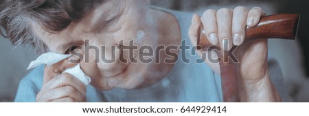 Older woman with dementia holding walking stick crying wiping tears