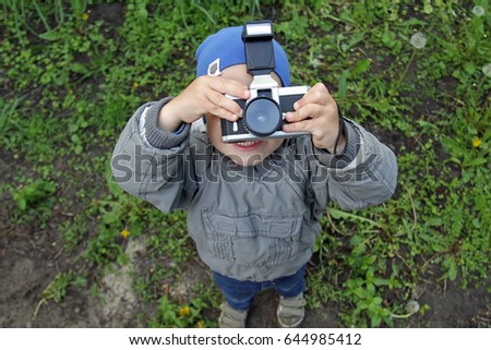 A little boy in a jacket and a blue hat is taking pictures of the sky. Young photographer view from above. The kid looks through the lens up.