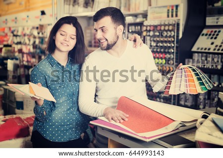Young family couple examining color scheme in paint supplies shop. Focus on man