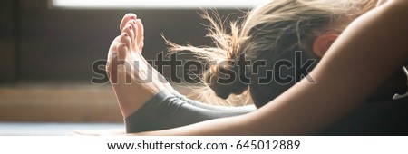 Young woman practicing yoga, sitting in Seated forward bend exercise, paschimottanasana pose, indoor, home interior background, close up. Horizontal photo banner for website header design  Royalty-Free Stock Photo #645012889