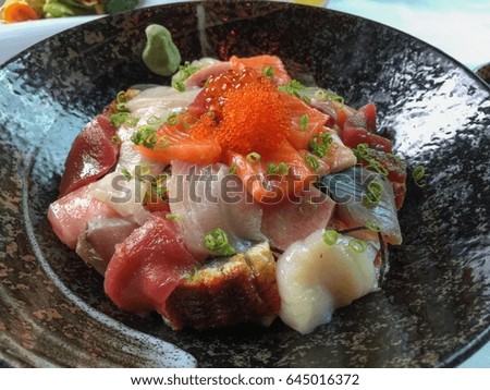 Japanese sashimi mixed raw fishes on ceramic plate with salmon roes on top and garnished with cut spring onions