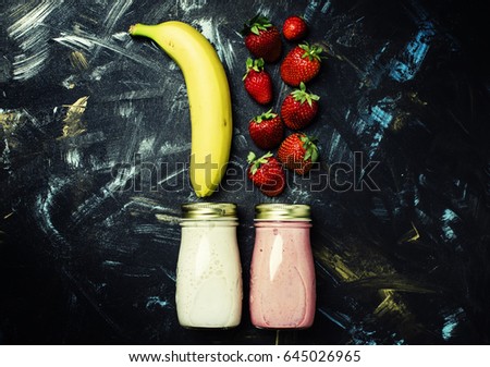 Food background, smoothies from strawberries and banana in small bottles, dark background, top view, flat lay