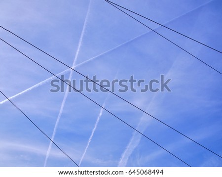 Airplane contrails on blue sky with tram and electric bus conductor wires.