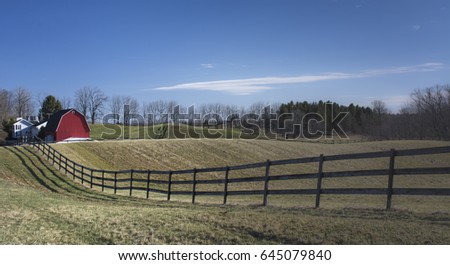 Landscape picture of a farm field with a fence and farmhouse and a barn in the distance.