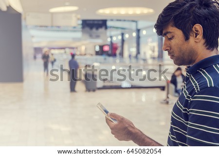 Young handsome man holding phone in the shopping mall. Indian man using phone.
