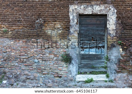 Old wooden door with blue cracked planks and damaged paint on a brick and stone wall in retro style with free space on the left side