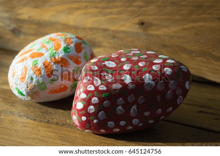 Hand painted decorative pebbles in green, white. orange and red on wood background bathed in sunlight