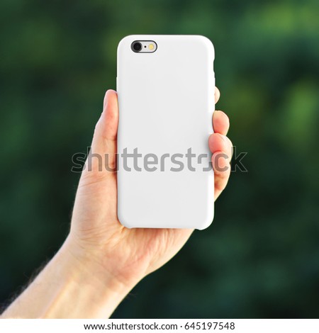 Smart phone on the blurred background of the park in a white plastic case back view. Smart phone in man's hand. Template of phone case Royalty-Free Stock Photo #645197548