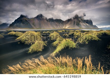 Vestrahorn, Iceland - dramatic sky over black sand beach and green grass with mountains in background