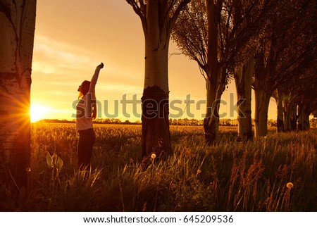 A woman with red curly hair on background of dawn in morning. Red-haired girl with pale skin bright unusual appearance and red lips and thin waist in the field on background of rising sun in morning.