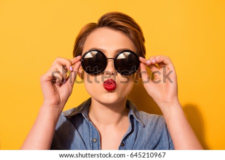 Kiss for you! Fashionable young cute girl in trendy sunglasses sends a kiss against bright yellow background, she holds spectacles with her hands Royalty-Free Stock Photo #645210967