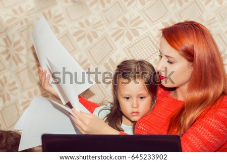 Mother with her child calculating home expenses. Busy Mother With child Running Business From Home looking at bank statement contract papers while kid looking cartoons on laptop sitting on bed