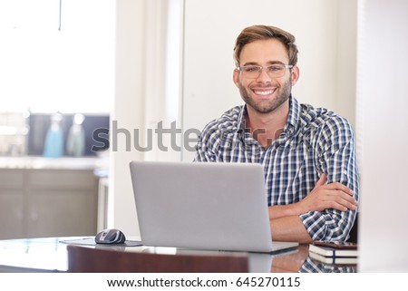 young caucasian man looking into the camera with a big smile while sitting behind his notebook on a bright spring morning with a joyful energy Royalty-Free Stock Photo #645270115