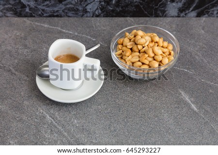 Cup of coffee and roasted nuts on a marble table.