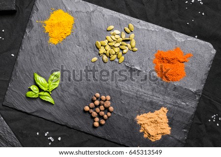 Large selection of different colorful contrast spices and seeds on slate against black background

