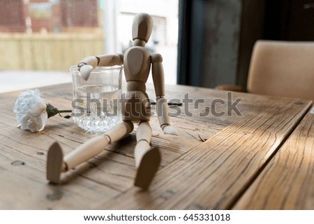 a wood man is sitting and put the arm on the glass of water