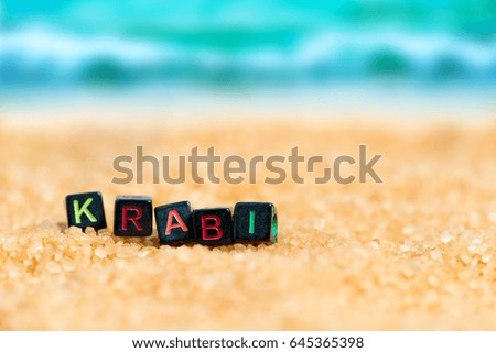 Multicolored word KRABI from black cubes in the sand on the background of beach and sea