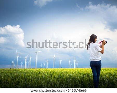 Young woman photographer taking pictures in a corn field and wind turbine