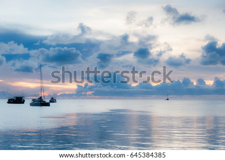 Soft focus of boats in the sea surface amidst dark clouds at sunset.