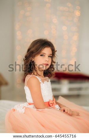 Little beautiful girl with brown hair in a Peach-colored dress. Poses for a photographer