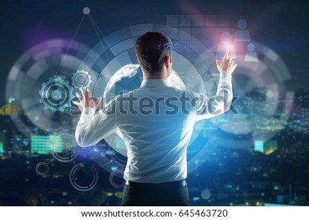 Back view of young businessman pressing abstract digital buttons on night city background